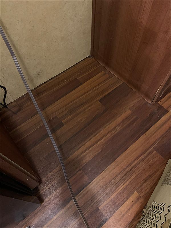 Dark wood-look floor meets light beige wall and dark wood cabinet corner; gray cable runs diagonally.