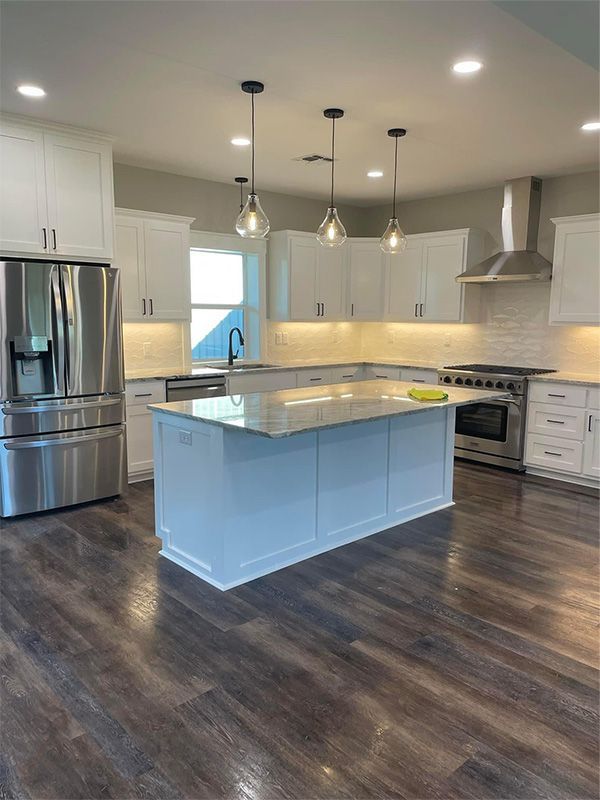 Bright white kitchen with a large island, stainless steel appliances, and dark wood-look flooring.