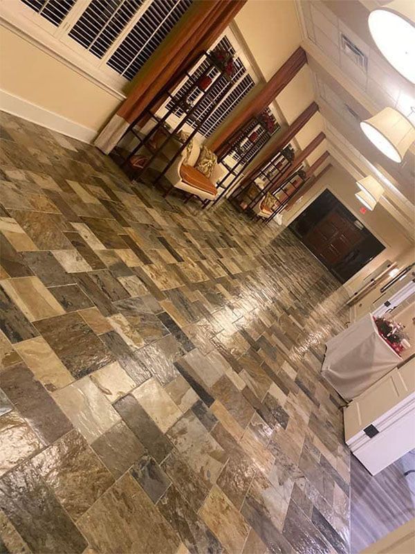 Slate tile floor in a long hallway with overhead lights, open windows, and tables.