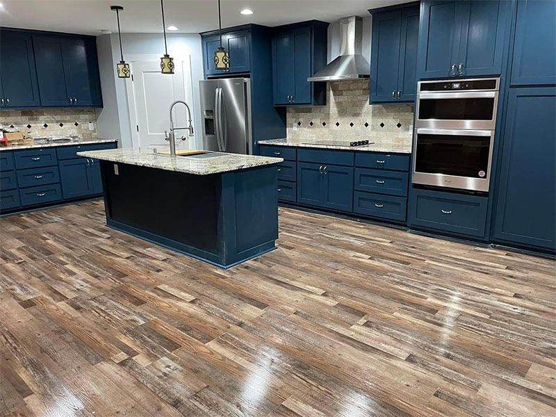 Blue kitchen cabinets with island and stainless steel appliances, set in a kitchen with wood-look flooring.