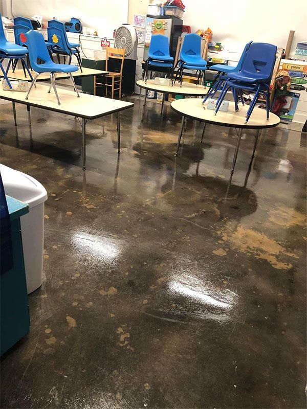 Classroom with tables, blue chairs stacked on them. Brown floor with a lighter dusty substance.