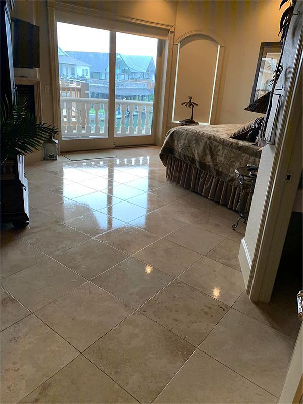 Bedroom with beige tiled floor, bed, balcony doors, and natural light.