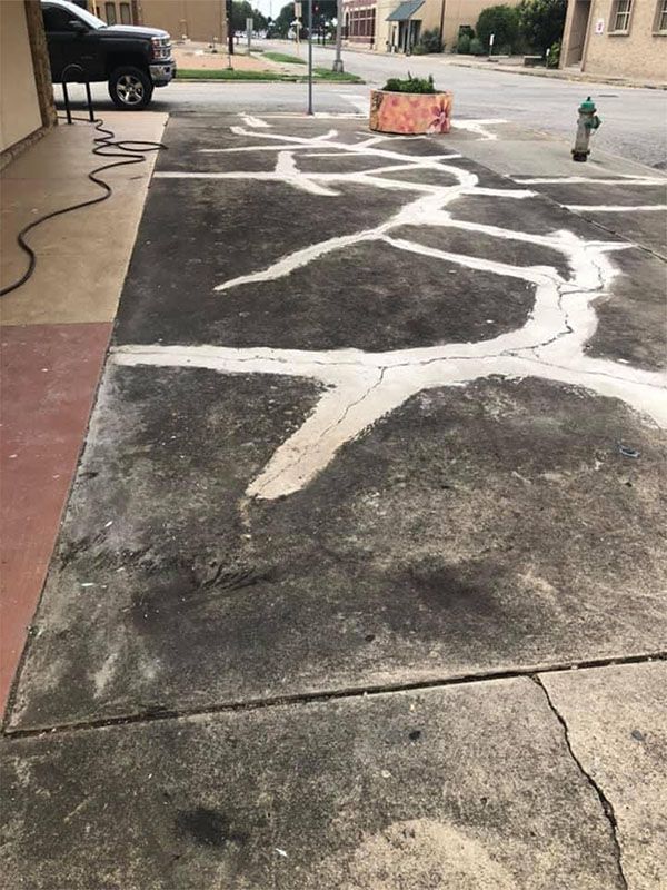 Cracked concrete sidewalk filled with white sealant, street view.