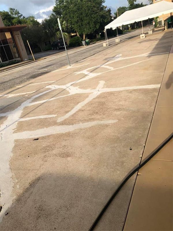 Concrete with white painted lines, possibly for parking or event space, with a tent in the background.