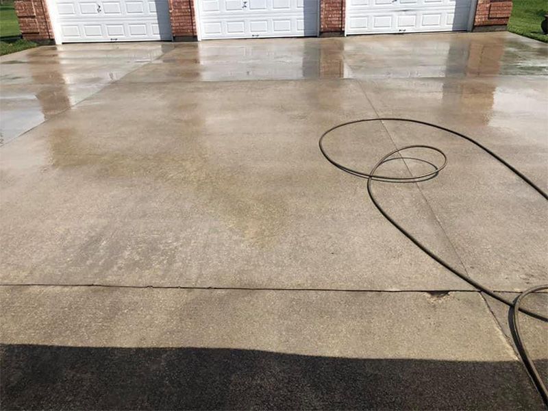 Wet concrete driveway in front of a garage with three doors; a black hose lies on the surface.