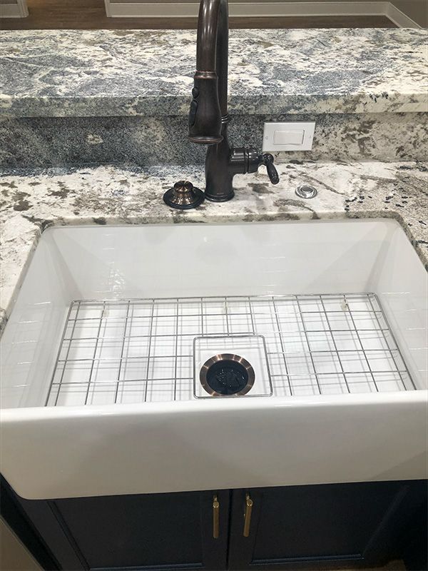 White farmhouse sink with metal grid and dark bronze faucet, set on granite countertop.