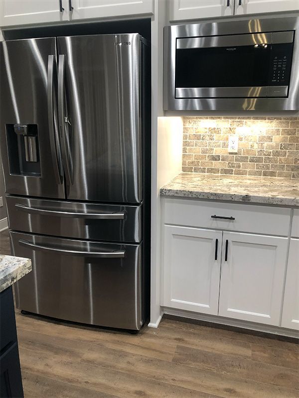 Stainless steel refrigerator and microwave in a white kitchen.