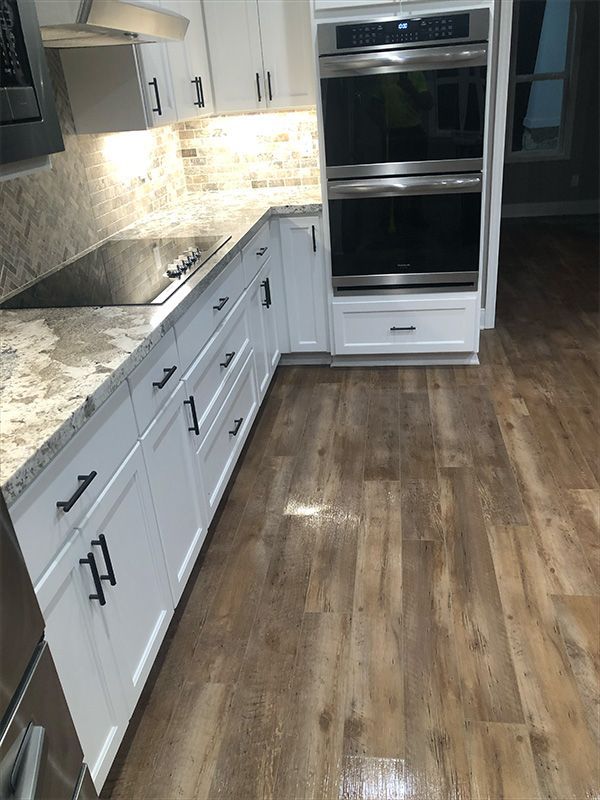 Modern kitchen with white cabinets, dark hardware, granite countertops, and wood-look flooring. Double ovens are on the right.