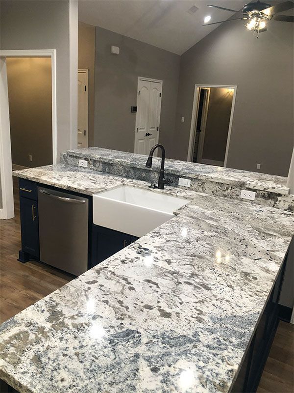 Kitchen island with granite countertop, stainless steel dishwasher, and farmhouse sink.