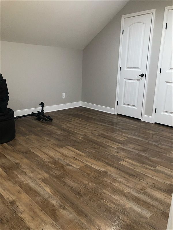 Empty room with light brown wood-look flooring, gray walls, white trim and doors.