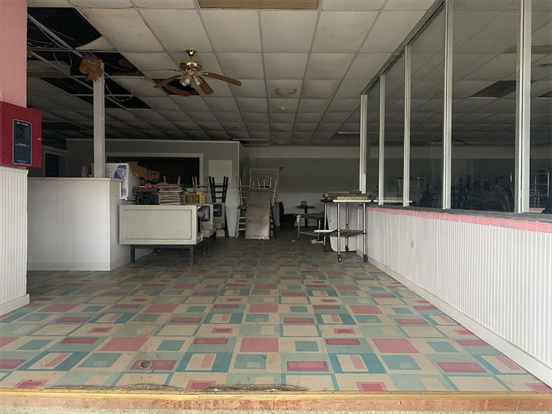 Interior view of an abandoned diner. Pastel pink and blue tile floor, peeling ceiling, empty space, and dirty windows.