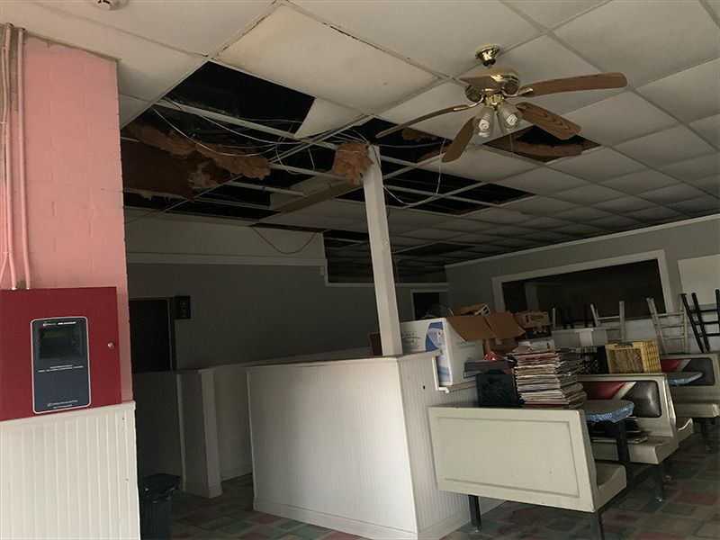 Interior of a building with severe ceiling damage, a white counter, and a ceiling fan.