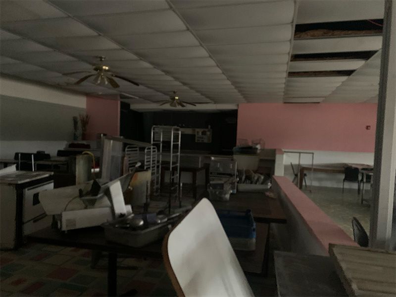 Interior view of a dilapidated restaurant, kitchen equipment scattered, pink walls, ceiling damage.