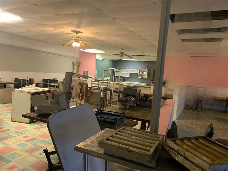 A cluttered, partially renovated room with tables, chairs, and equipment, likely a former restaurant.