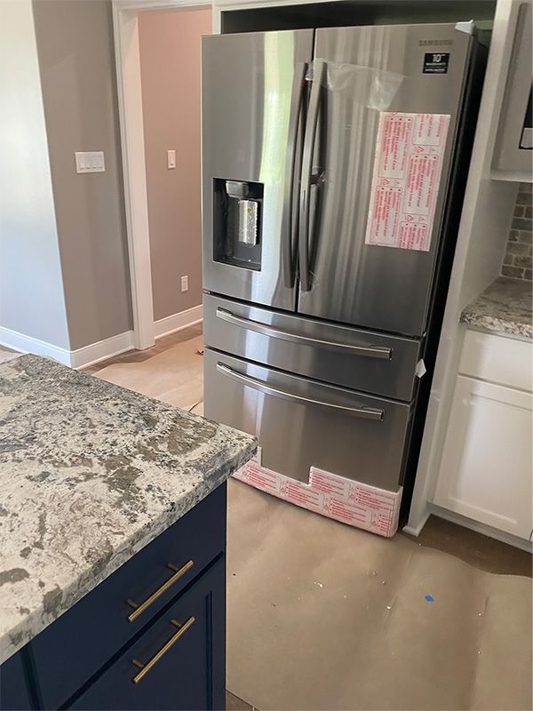 A stainless steel refrigerator is in a kitchen, next to white cabinets. A dark blue cabinet with granite is in the foreground.