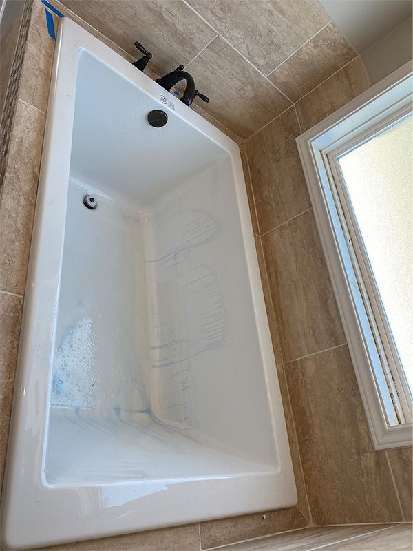 White bathtub in a bathroom with tan tiled walls and a window; a black faucet is visible.