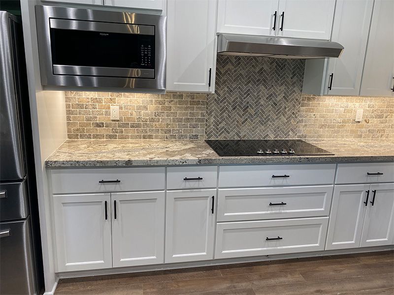 White kitchen with stainless steel appliances, light backsplash, and granite countertops.