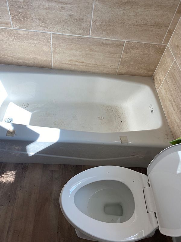 White bathtub and toilet in bathroom with beige tile walls and wooden floor.