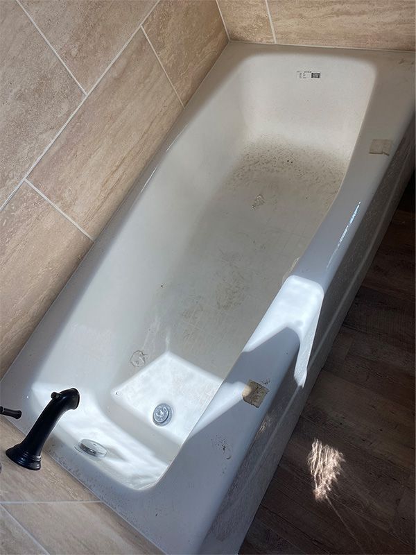 White bathtub with black faucet in a bathroom with light brown tile.