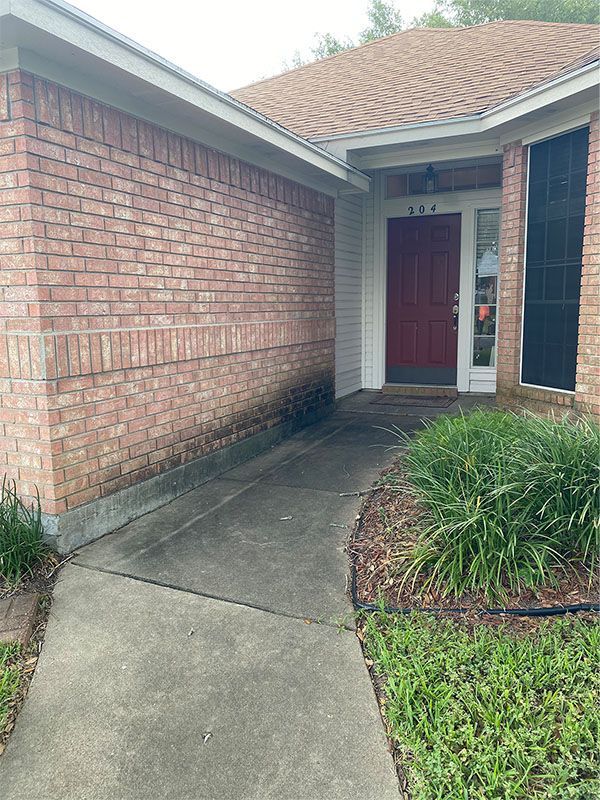 Brick house exterior with a sidewalk leading to a red door. Dark stain visible on the brick near the walkway.