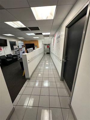 Office hallway with white tile floor, cubicles on the left, and a long wall with notices on the right.