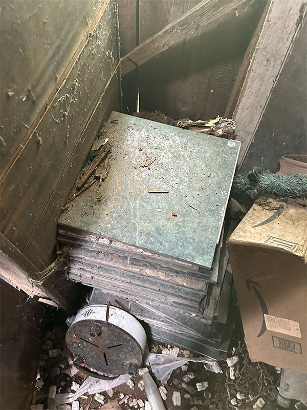 Stack of green-tinged tiles inside a dusty, dark alcove with debris and cardboard box.