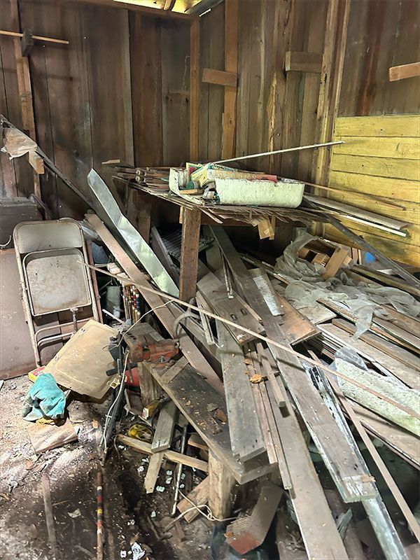 Cluttered shed interior with wood planks, metal, and a folding chair. Wooden walls and a small shelf are visible.