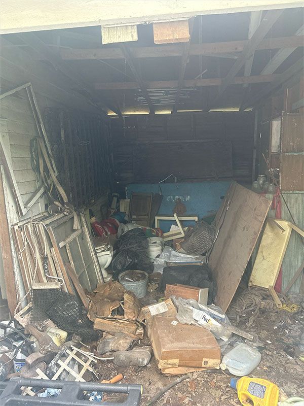 Cluttered garage filled with debris: wood, windows, bags, and miscellaneous items.