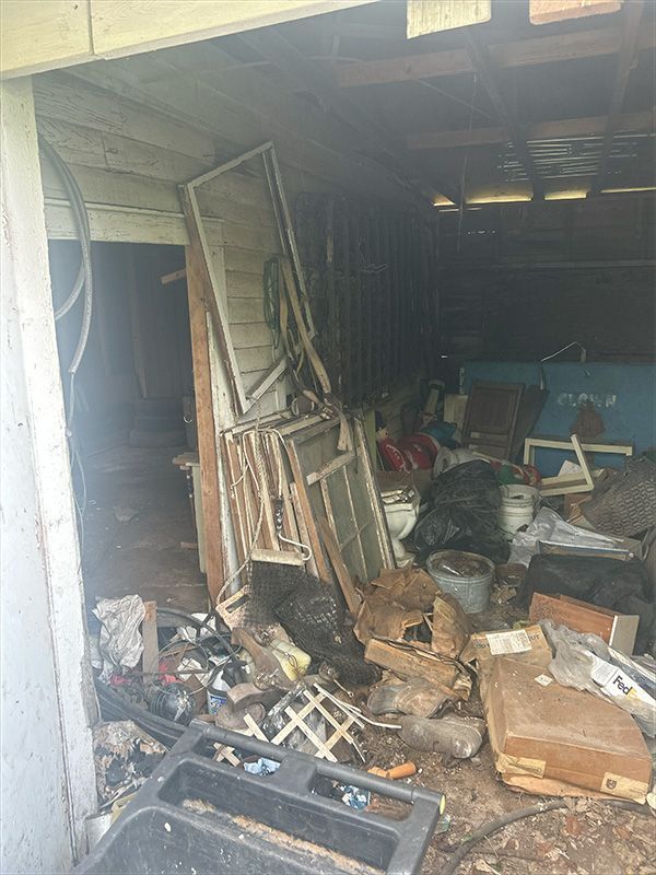 Messy storage room filled with junk, including windows, trash bags, and debris.