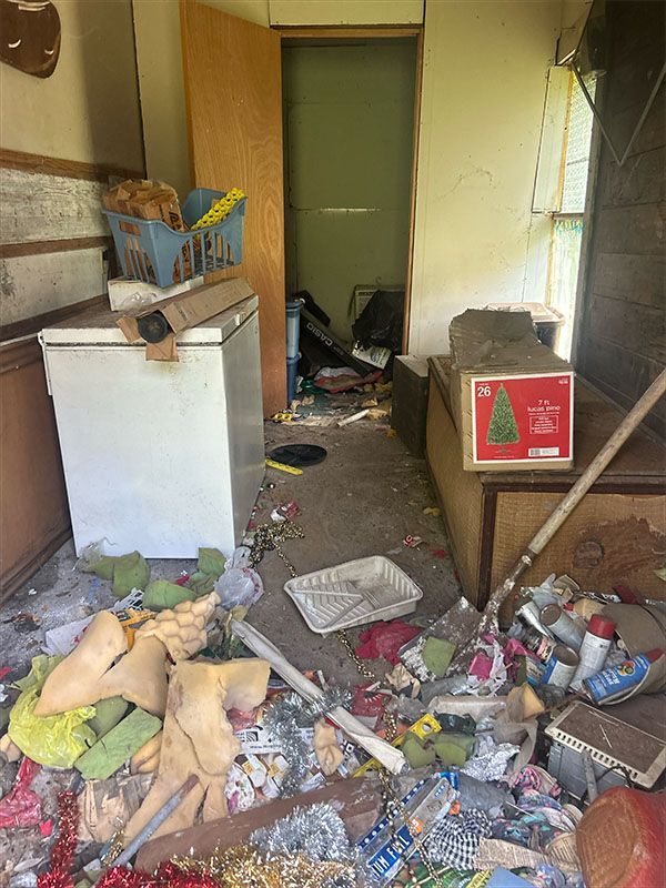 Messy room with debris on the floor; open doorway; refrigerator, boxes, and trash.