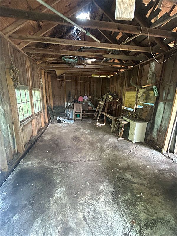 Dilapidated wooden shed interior with debris, furniture, and natural light.