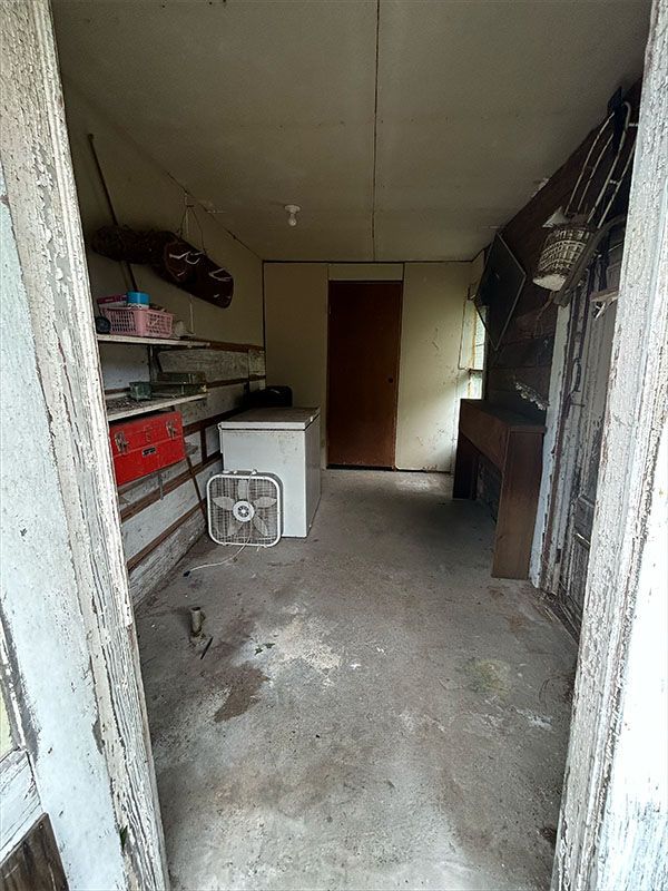 View from doorway into a small, cluttered room with a refrigerator, fan, and storage shelves.