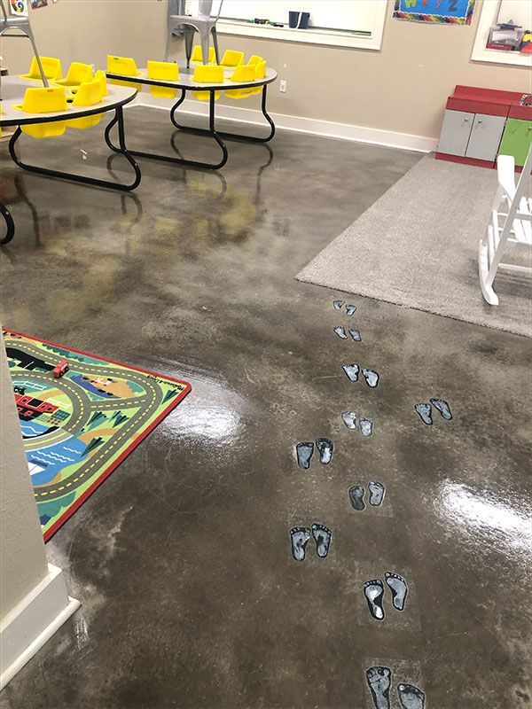 Footprint path on a polished concrete floor in a children's playroom; small tables and a rug are nearby.