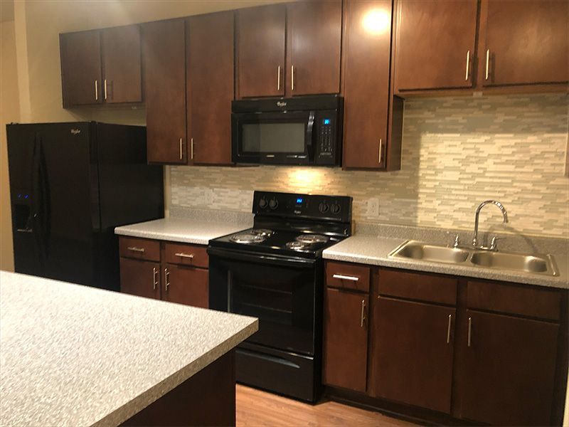 A kitchen with dark wood cabinets, black appliances, light countertops, and a textured backsplash.