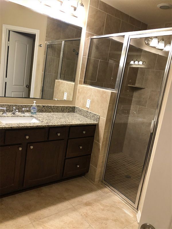 Bathroom with dark brown cabinets, granite countertop, large shower with glass doors, and a mirror.