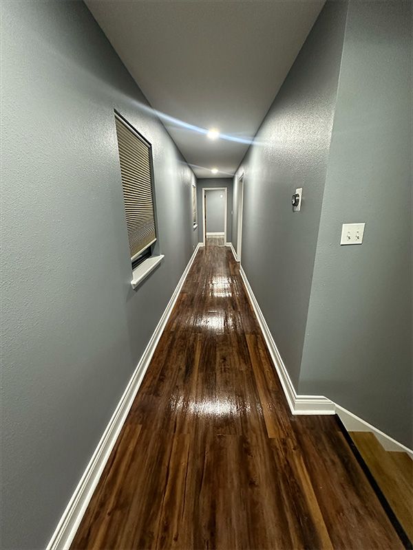 Long, narrow hallway with gray walls, wood-look floor, and recessed lighting.