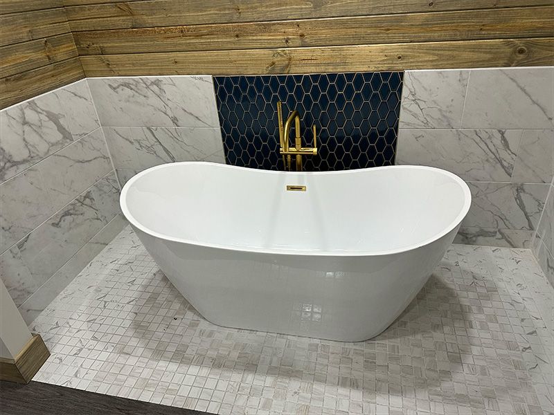 A white freestanding bathtub with gold fixtures set against marble and mosaic tiles, with a wood beam above.