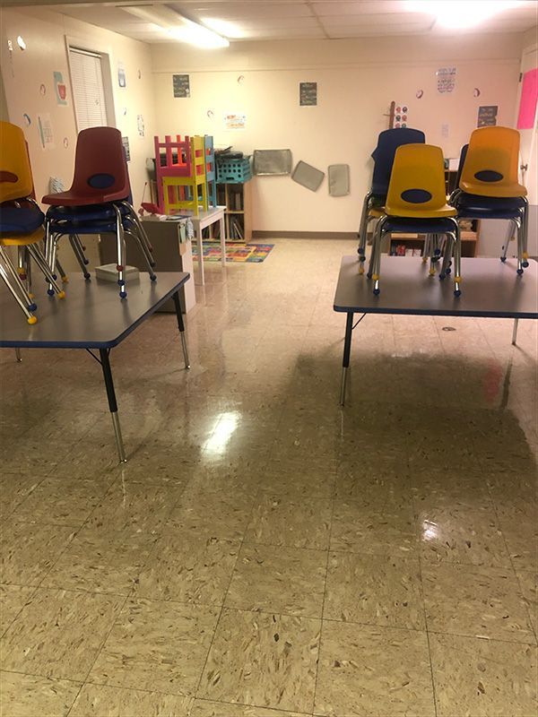 Empty classroom with two tables, chairs on top, colorful play structures, and a tiled floor.