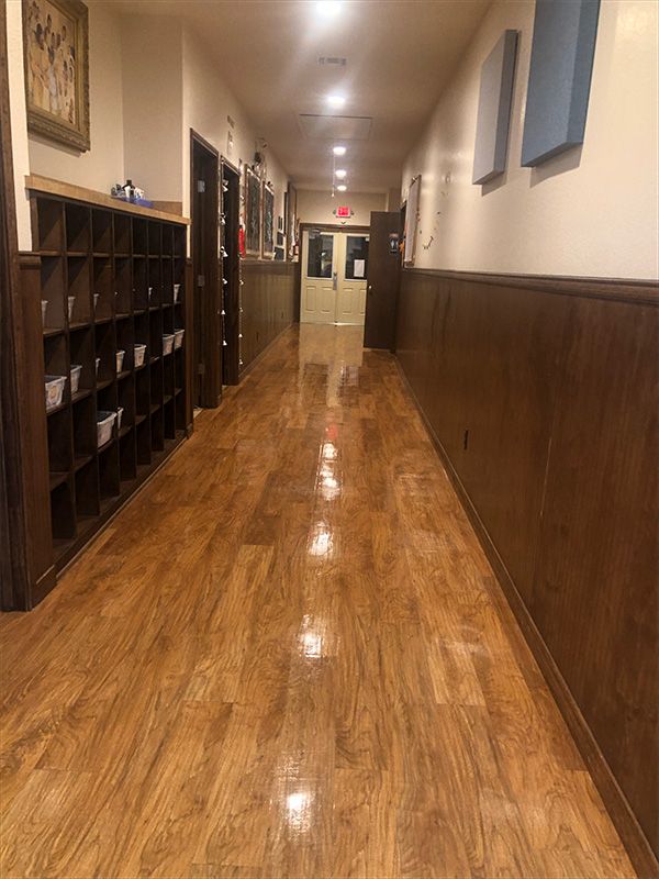 Long hallway with wood-look flooring, lockers on the left, wood paneling, and a door at the end.