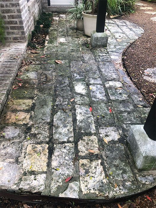 Brick walkway with dark patches and debris, leading to a curved gravel area.