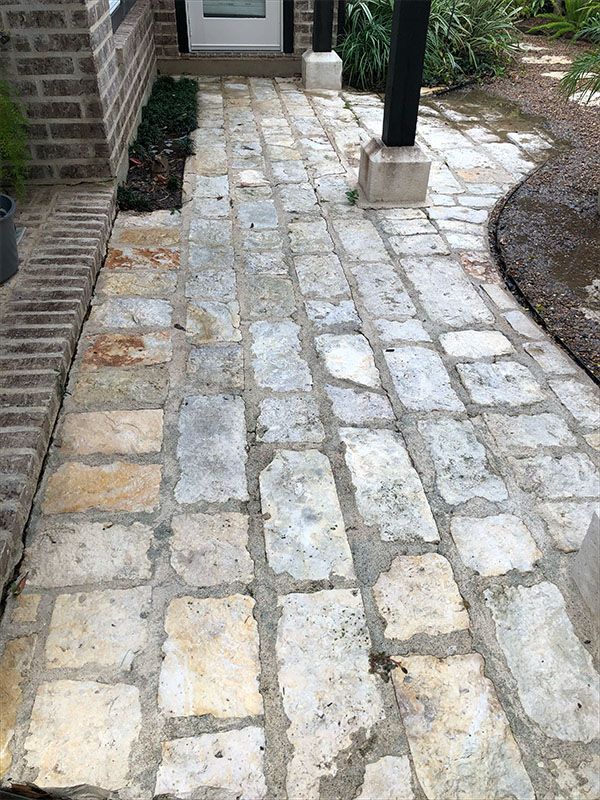 Stone path leading to a front door, edged by brick and greenery. Light grey and yellow stone.