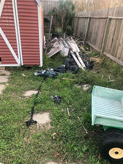 Backyard scene with shed, trash, overgrown grass, and a small green wagon.