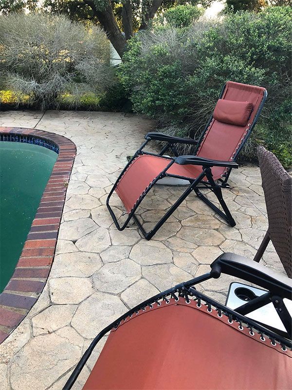 Lounge chair by a pool. Red chair on stone patio, dark frame, brick pool edge, green water, foliage in background.