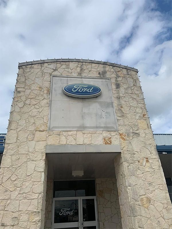 Ford dealership building with the Ford logo, against a cloudy sky.