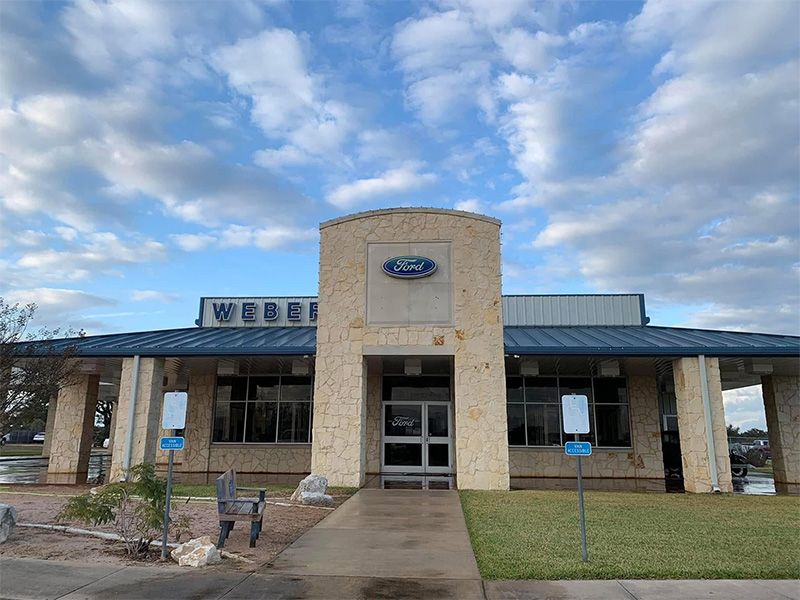 Weber Ford dealership building with Ford logo, blue accents, and cloudy sky.