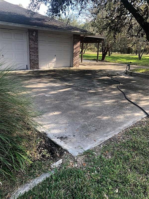 Concrete driveway in front of a garage with two doors, and a small ditch at the edge, shaded by trees.