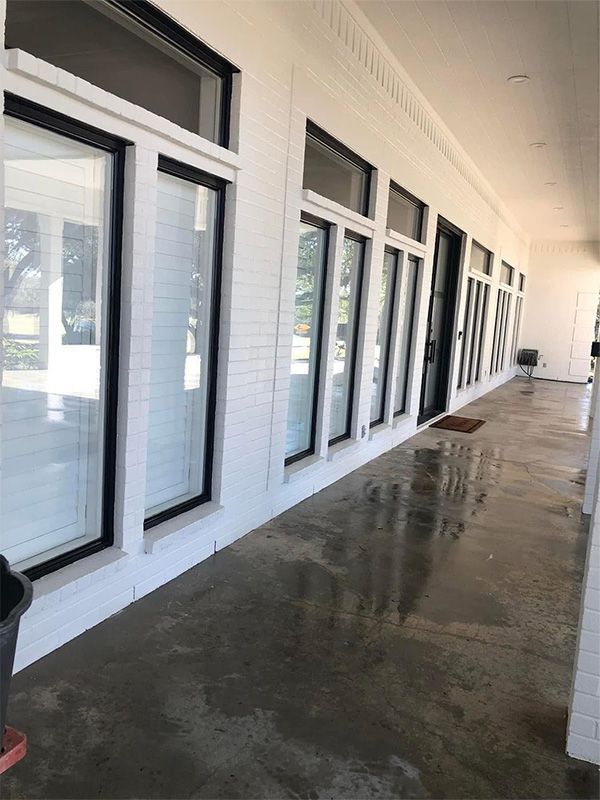 Exterior view of a white building with large black-framed windows and a wet, concrete walkway.