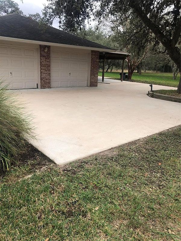 Beige concrete driveway in front of a garage, with a grassy lawn.