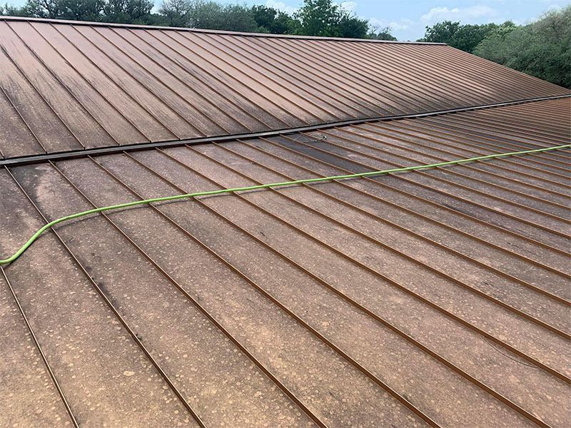 Copper-colored metal roof with a green hose running across it, under a bright blue sky.