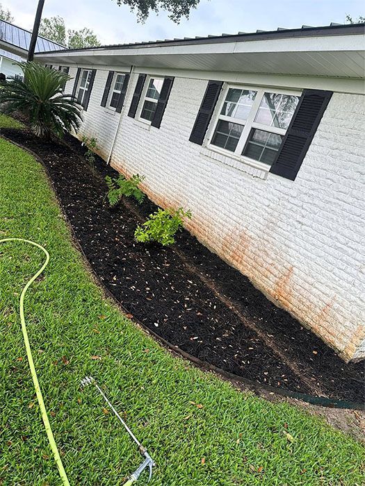 Black mulch lines a house foundation with green grass on the left.